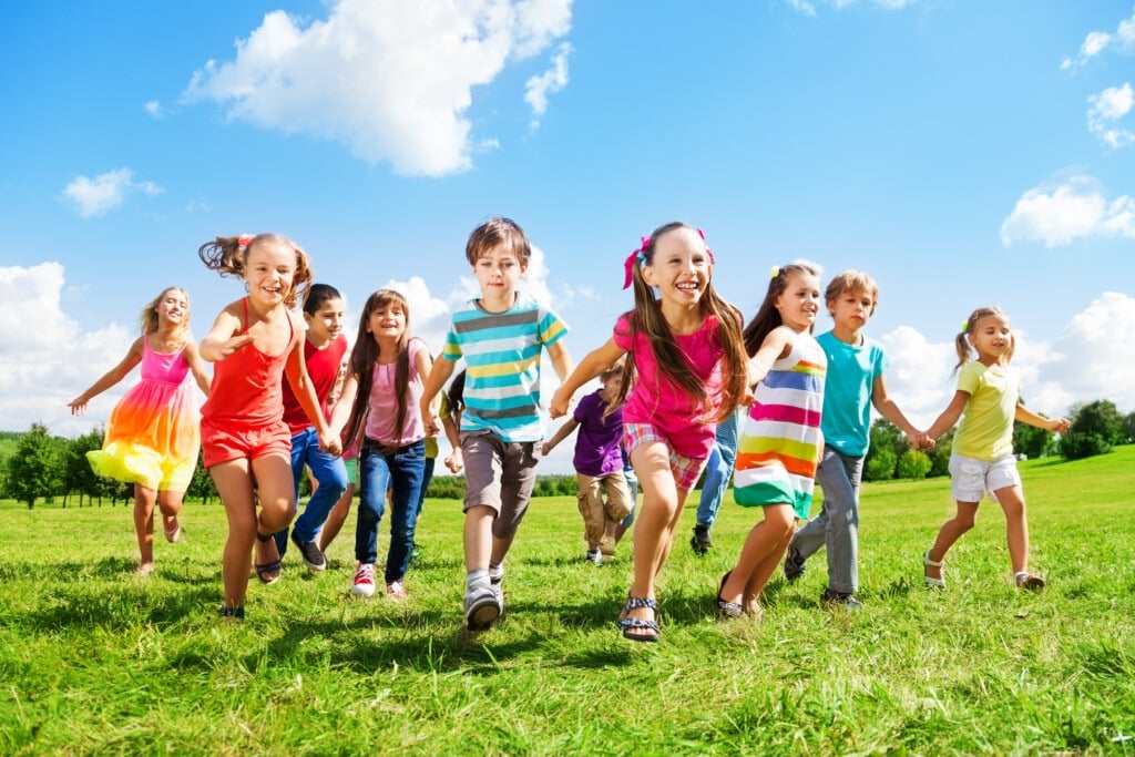A group of smiling children in colorful clothes run together across a grassy field under a bright blue sky, enjoying a sunny day outdoors during ABA near Houston TX.